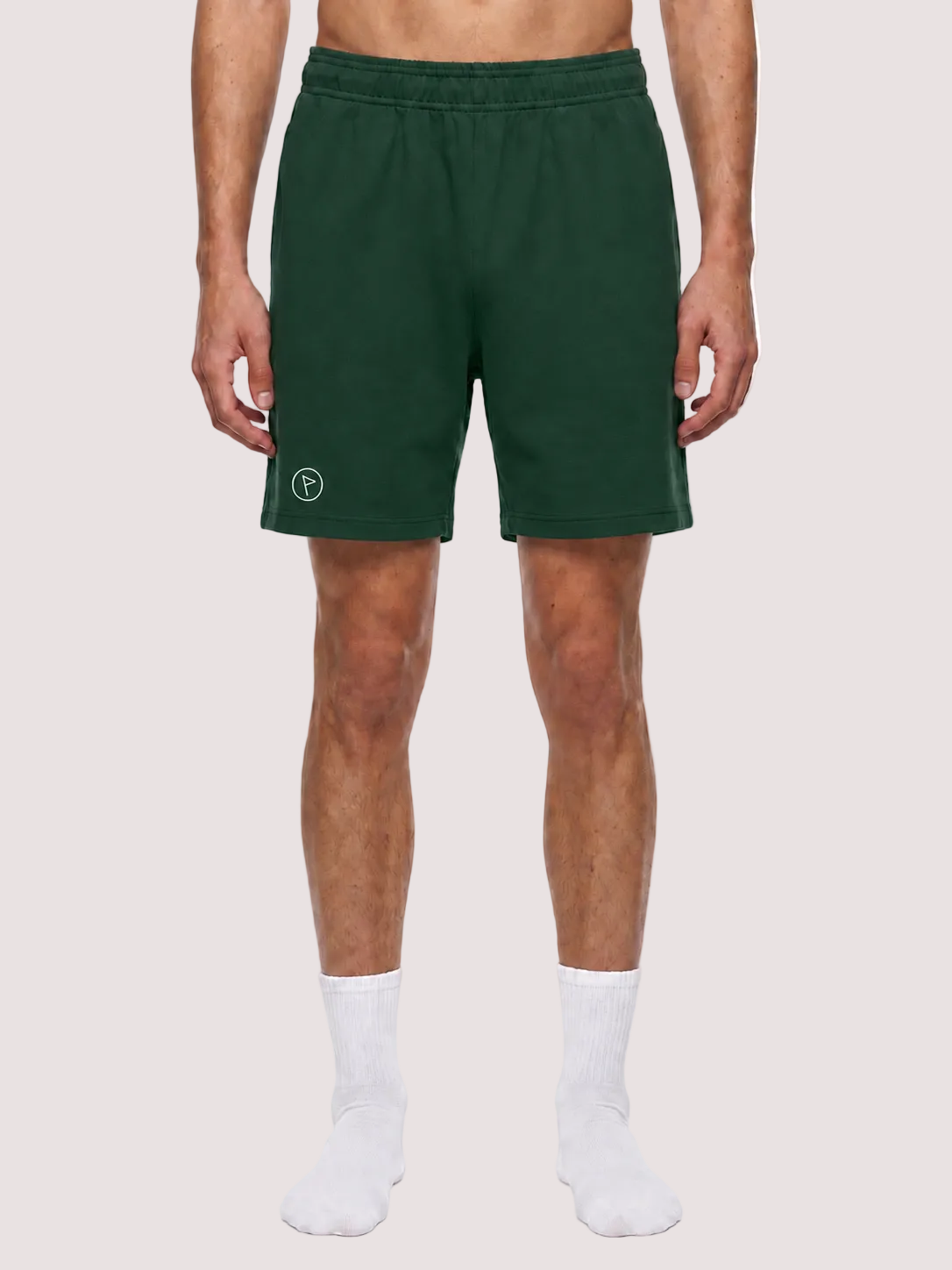 A model from the waist down wearing dark green athletic shorts with a small white circular logo on the left leg, paired with white socks, against a plain white background.